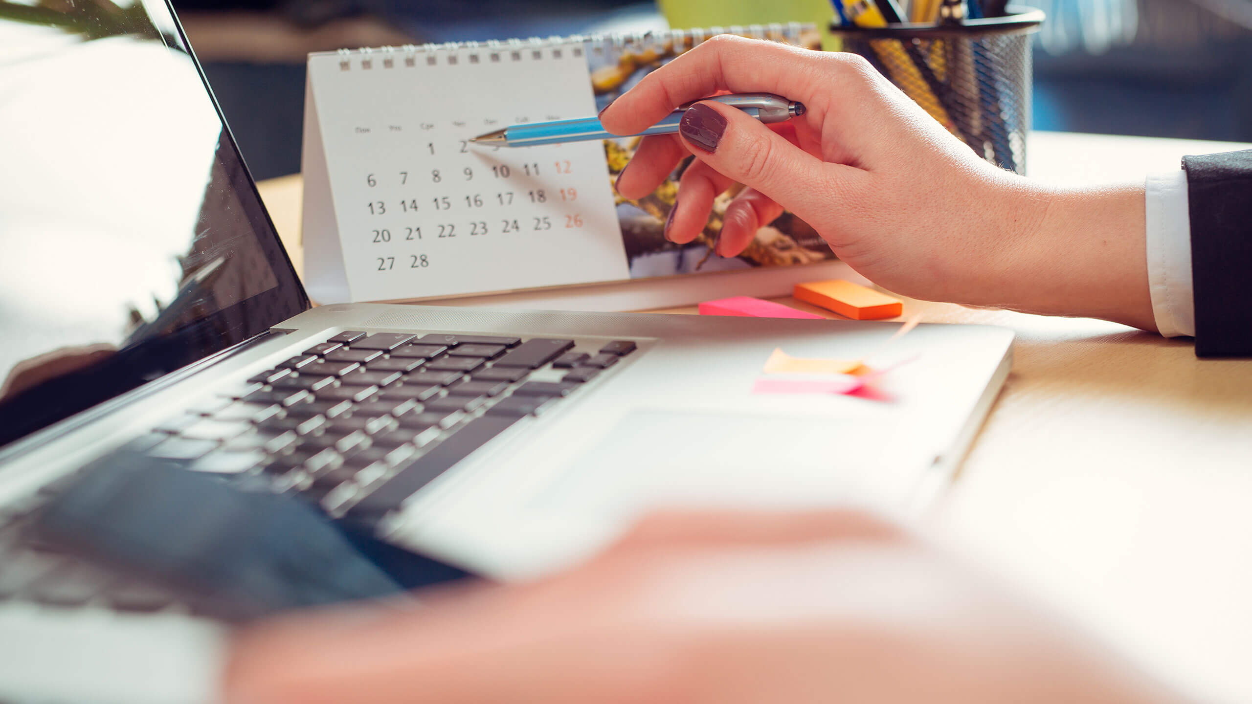 Kuvituskuva: Nainen työpöydän ääressä osoittaa kynällä pöytäkalenteria.