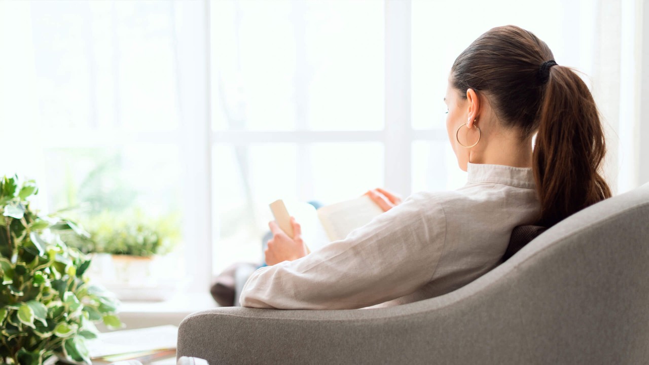 Kuvituskuva: Nainen olohuoneen sohvalla lukemassa kirjaa.