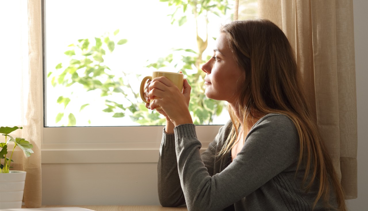 Kuvituskuva: Nainen istuu keittiössä, juo kahvia ja katsoo ikkunaan