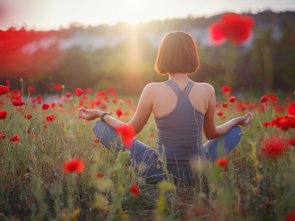 A beautiful woman meditates on a poppy field at sunset. Wellness well-being happiness concept.